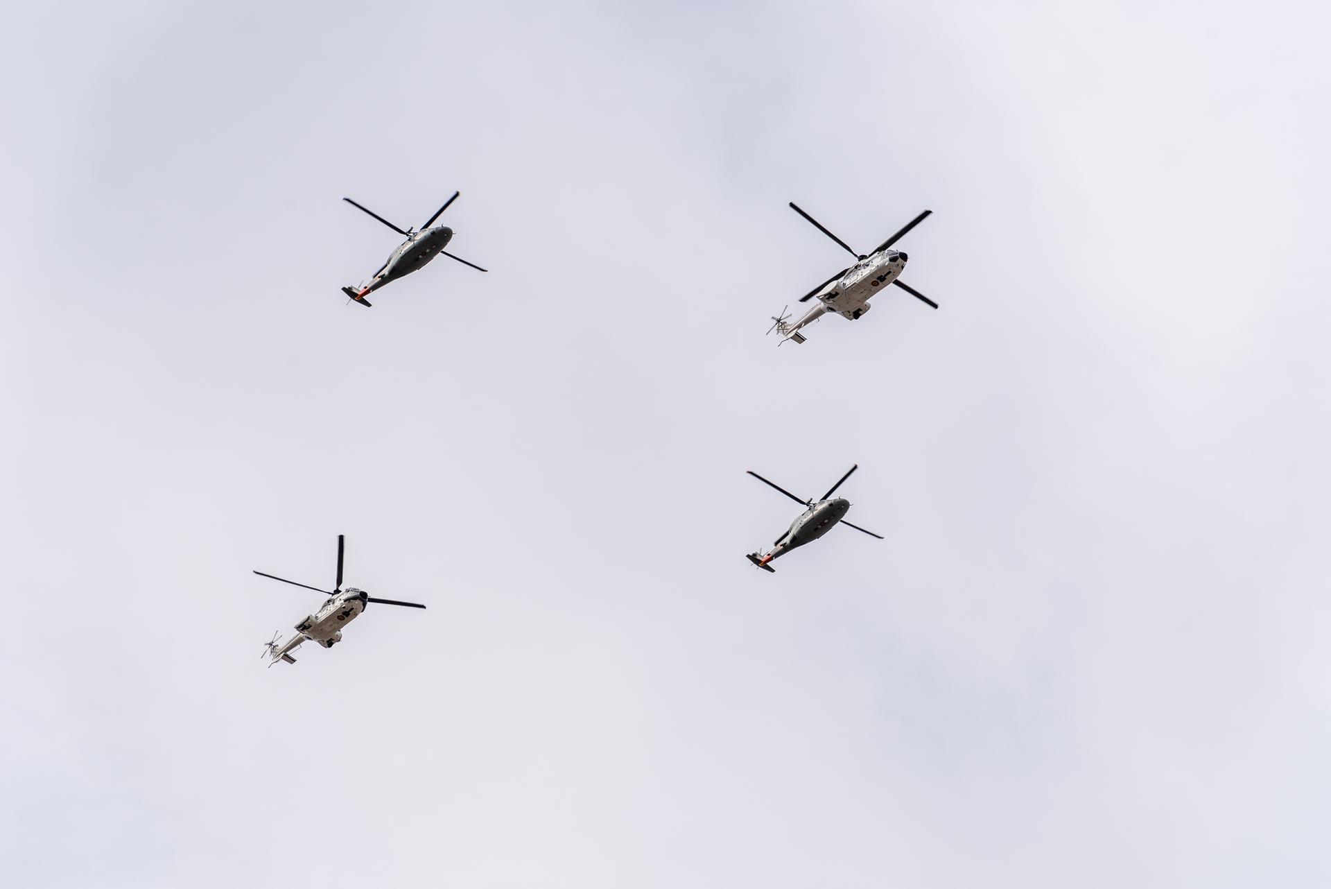 Four helicopters seen from below against a grey sky